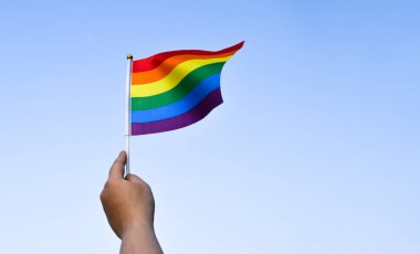Gururlu gökkuşağı lgbt gay bayrakları ellerinde ve bulutlu ve mavi gökyüzüne karşı rüzgarda sallanıyorlar. Lgbtq + gurur ayı konseptinde kutlama, bayraklar üzerine yumuşak ve seçici odaklanma.