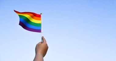 Gururlu gökkuşağı lgbt gay bayrakları ellerinde ve bulutlu ve mavi gökyüzüne karşı rüzgarda sallanıyorlar. Lgbtq + gurur ayı konseptinde kutlama, bayraklar üzerine yumuşak ve seçici odaklanma.
