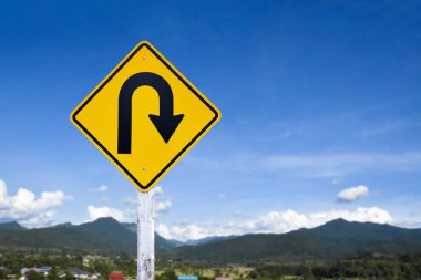 Trafik işareti: Kırsal yolun yanındaki çimento direğinde sağa U dönüşü işareti, beyaz bulutlu mavi arka plan, boşluğu kopyala.