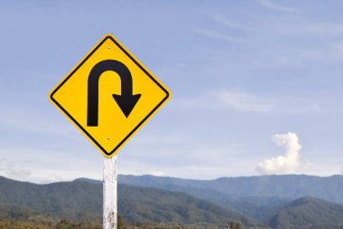 Trafik işareti: Kırsal yolun yanındaki çimento direğinde sağa U dönüşü işareti, beyaz bulutlu mavi arka plan, boşluğu kopyala.