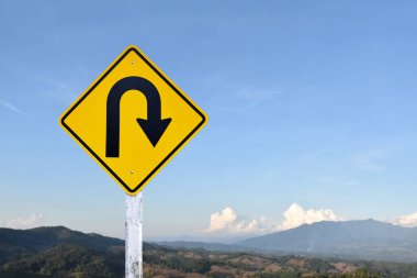 Trafik işareti: Kırsal yolun yanındaki çimento direğinde sağa U dönüşü işareti, beyaz bulutlu mavi arka plan, boşluğu kopyala.