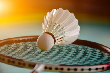 Krem beyazı badminton servis aracı ve kapalı badminton kortunda yeşil zemin üzerinde neon ışıklı raket, bulanık badminton arka plan, kopyalama alanı.