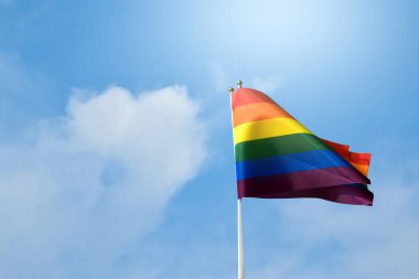 Gökkuşağı bayrağı, LGBT topluluğunun sembolü, bulutlu mavi bir arka planla rüzgarda sallanan. 