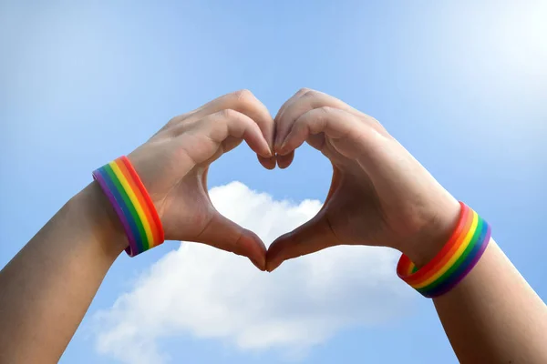 同性恋 同性爱情和同性恋关系概念 男性手拉手 带着同性恋自豪感彩虹意识腕带 带着蓝色背景的心形手势 — 图库照片