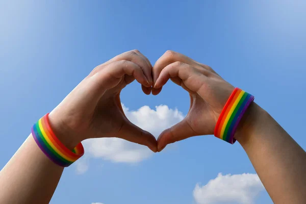 同性恋 同性爱情和同性恋关系概念 男性手拉手 带着同性恋自豪感彩虹意识腕带 带着蓝色背景的心形手势 — 图库照片