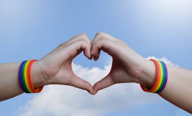 Igbt, eşcinsel aşk ve homoseksüel ilişkiler konsepti - gay gururlu erkek ellerine yakın gökkuşağı farkındalığı bileklikleri mavi arka planda kalp hareketi gösteriyor.