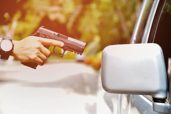 automatic 9mm pistol holding in hand of gun shooter and aming to the glassdoor of the car, concept for car robbery and vip protection, soft and selective focus.