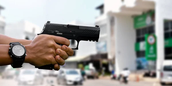 9mm automatic pistol holding in hands of shooter, blurred bank background, concept for security, bank robbery, gangster, bodyguard around the world. selective focus on pistol.