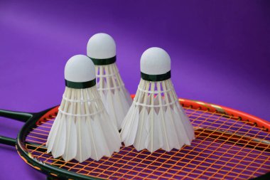 Beyaz kremalı badminton mekikleri ve raketleri mor zeminde, badminton kortunda fotokopi alanı, badminton spor aşığı ve dayanıklılık konsepti..