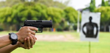 Otomatik siyah 9 mm 'lik tabanca nişancının elinde ve ilerideki hedef tahtasını hedef alıyor. İnsanları koruma, VIP koruyucusu ve gangsterler olmak için eğitme ve uygulama kavramı..