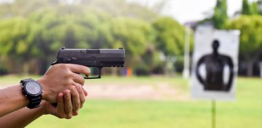 Otomatik siyah 9 mm 'lik tabanca nişancının elinde ve ilerideki hedef tahtasını hedef alıyor. İnsanları koruma, VIP koruyucusu ve gangsterler olmak için eğitme ve uygulama kavramı..