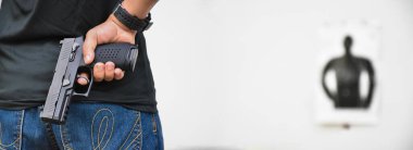 Otomatik siyah 9 mm 'lik tabanca nişancının sağ elinde ve ilerideki hedef tahtası önünde duruyor. İnsanları koruma, VIP koruyucusu ve gangster olmak için eğitme ve alıştırma yapma kavramı..