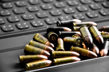 Pile of 9mm pistol bullets on taplet keyboard and screen, soft and selective focus, concept for learning types of bullets by using smart devices to search and store the database.