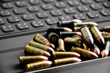 Pile of 9mm pistol bullets on taplet keyboard and screen, soft and selective focus, concept for learning types of bullets by using smart devices to search and store the database.