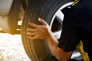 The car attendant is turning the car wheel back into the car's hub after the tire leak has been repaired, soft and selective focus on wheel, in motion.
