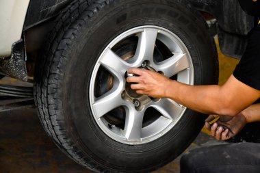The car attendant is turning the car wheel back into the car's hub after the tire leak has been repaired, soft and selective focus on wheel, in motion.