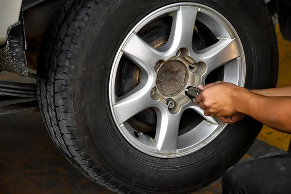 The car attendant is turning the car wheel back into the car's hub after the tire leak has been repaired, soft and selective focus on wheel, in motion.