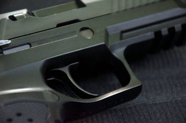 Siyah deri arka planda otomatik 9 mm 'lik tabanca tetik, yumuşak ve seçici odaklı..