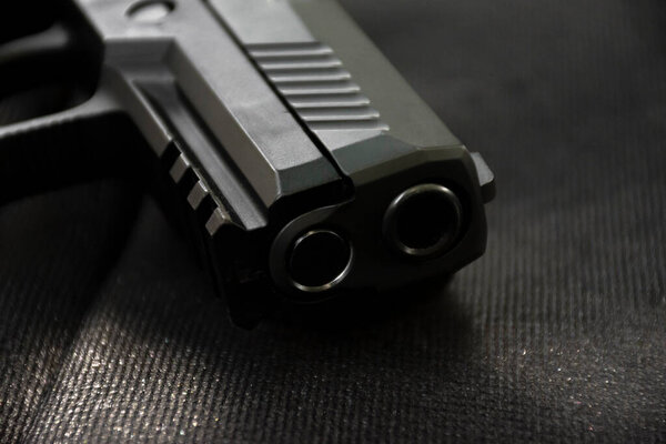 Automatic 9mm pistol gun muzzle on black leather background, soft and selective focus.