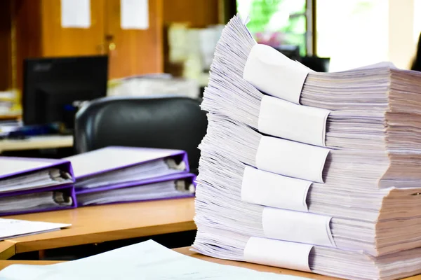 A pile of paper, an important, unfinished work, was piled up on a desk in an office, soft and selective focus.