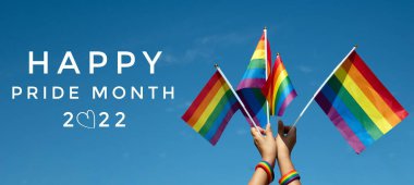 'HAPPY PRiDE MONTH 2022' on bluesky and rainbow flags background, concept for lgbtq+ celebrations in pride month, june, 2022. clipart