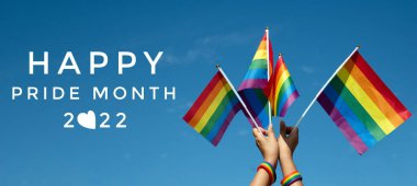 'HAPPY PRiDE MONTH 2022' on bluesky and rainbow flags background, concept for lgbtq+ celebrations in pride month, june, 2022. clipart