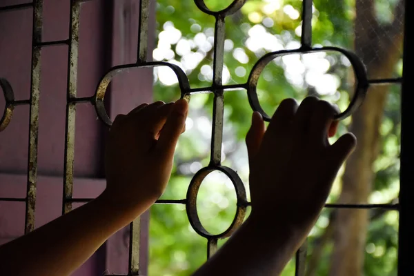 Both of the prisoners\' hands rested on steel braces attached to windows to prevent escaping through the windows in a detention facility or prisons, soft and selective focus on hands.