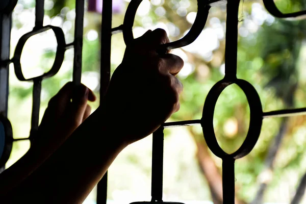 Both of the prisoners\' hands rested on steel braces attached to windows to prevent escaping through the windows in a detention facility or prisons, soft and selective focus on hands.