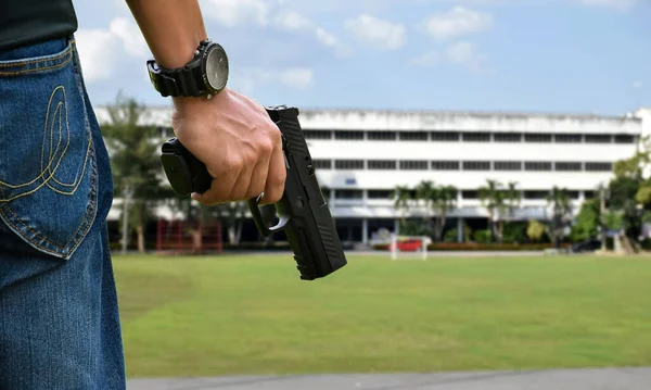 9mm pistol gun holding in right hands of shooter in front of the grass court with blurred office buildings background, concept for security, bodyguard, ganster, mafias, robbery and property protection