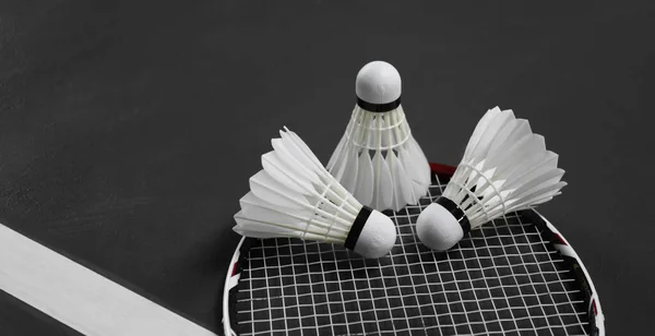 White cream badminton shuttlecock  and rackets on dark floor of the indoor badminton court, soft and selective focus on shuttlecock, concept for badminton sports around the world.