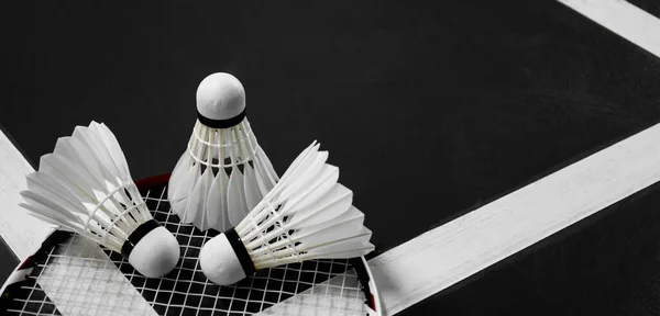 White cream badminton shuttlecock  and rackets on dark floor of the indoor badminton court, soft and selective focus on shuttlecock, concept for badminton sports around the world.