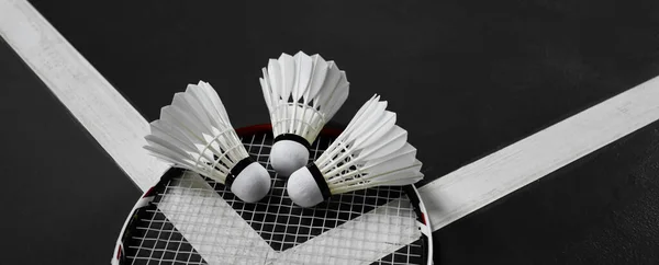 White cream badminton shuttlecock  and rackets on dark floor of the indoor badminton court, soft and selective focus on shuttlecock, concept for badminton sports around the world.