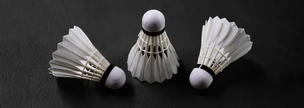 White cream badminton shuttlecock  and rackets on dark floor of the indoor badminton court, soft and selective focus on shuttlecock, concept for badminton sports around the world.