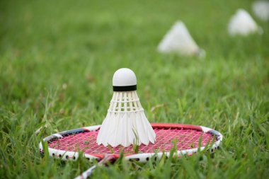 Beyaz kremalı badminton topu ve badminton raketi çimenli arka planda bulanık mekik penisleri açık havada badminton oynamak için konsept, yumuşak ve seçici odaklanma.