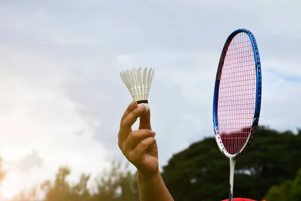 Badminton outdoor playing, badminton racket and shuttlecock holding in hand of player, blurred outdoor grasslawn and park background, soft and selective focus on shuttlecock and racket.