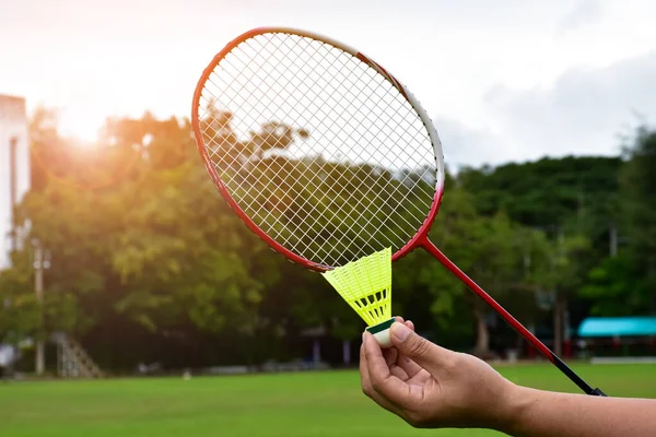 Badminton outdoor playing, badminton racket and shuttlecock holding in hand of player, blurred outdoor grasslawn and park background, soft and selective focus on shuttlecock and racket.