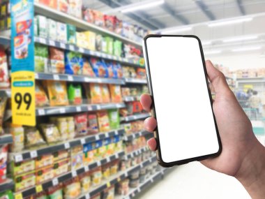 Mockup Mobile phone holding in hand with blurred supermarket background, concept for using smart devices with online shooping apps, online transactions and checking the goods price at home, at work, on application and in daily life.