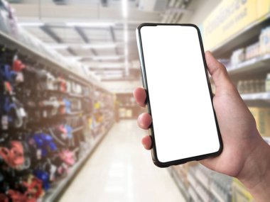 Mockup Mobile phone holding in hand with blurred supermarket background, concept for using smart devices with online shooping apps, online transactions and checking the goods price at home, at work, on application and in daily life.