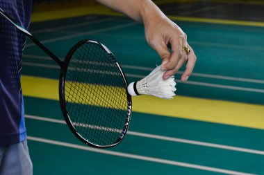 Badminton raketi ve eski beyaz mekikçik oyuncunun elinde tutarken ilerideki ağda servis yaparken, bulanık badminton sahası geçmişi ve seçici odaklanma