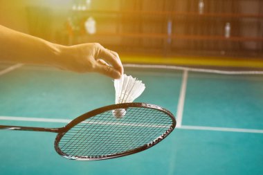 Badminton oyuncusu, raketi ve beyaz kremalı mekikçiyi sahanın diğer tarafına götürmeden önce kalenin önünde tutuyor..