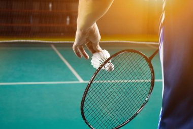 Badminton oyuncusu, raketi ve beyaz kremalı mekikçiyi sahanın diğer tarafına götürmeden önce kalenin önünde tutuyor..
