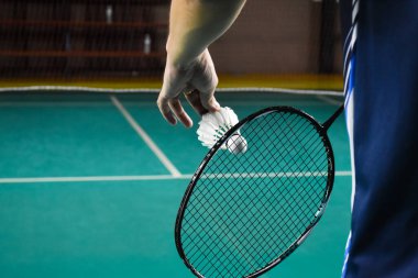 Badminton oyuncusu, raketi ve beyaz kremalı mekikçiyi sahanın diğer tarafına götürmeden önce kalenin önünde tutuyor..