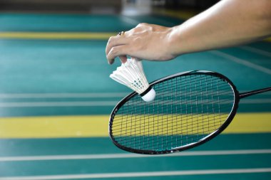 Badminton oyuncusu, raketi ve beyaz kremalı mekikçiyi sahanın diğer tarafına götürmeden önce kalenin önünde tutuyor..