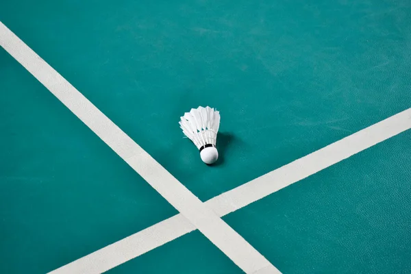 Cream white badminton shuttlecock on green floor in indoor badminton court, blurred badminton background, copy space