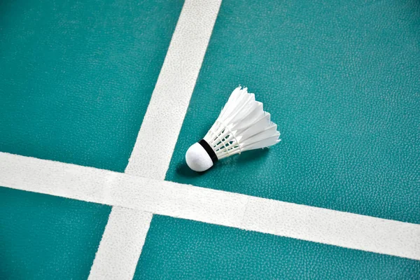 Cream white badminton shuttlecock on green floor in indoor badminton court, blurred badminton background, copy space