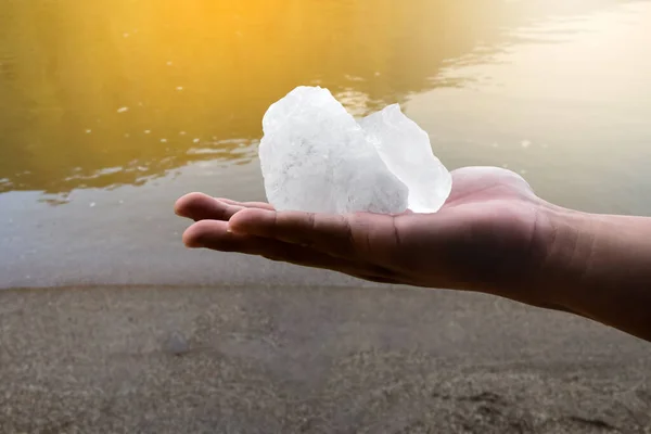 White alum bar holding in hand with cloudy water, concept for using alum to sway or swing the cloudy water to be clean and clear before using it in human daily life, soft and selective focus.