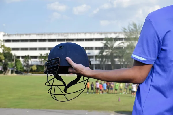 Cricket helmet holding in hand of cricketer, blurred green grass cricket field, concept for using cricket sport equipment in training.