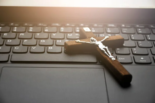 Wooden cross necklace on notebook keyboard, soft and selective focus on cross necklace.