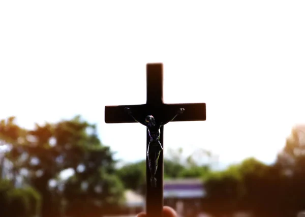 イエスの像が腕で十字架につけられた黒い木の十字架 その背後には アジア諸国の学校の校舎があり 柔らかく選択的な焦点 — ストック写真