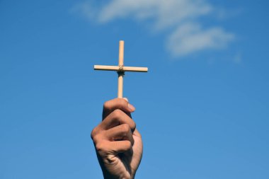 Bulutlu ve mavi gökyüzü arkaplanıyla el ele tutuşan küçük ahşap haç, aşk, umut, doğruluk, inanç, İsa 'ya inan, yumuşak ve seçici odaklanma konsepti.